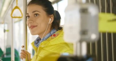 Kulaklık takmış, akıllı telefondan müzik dinleyen ve otobüsle bir yerlere giden mutlu, genç, beyaz bir kız. Telefondan oyuncu kullanan neşeli kadın tramvay yolcusu..