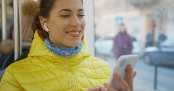 Close up de alegre menina bonita branca em fones de ouvido bluetooth ouvir música no smartphone e sorrindo. Passanger feminino alegre de transporte público usando jogador no telefone . — Vídeo de Stock