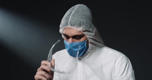 Уставший молодой кавказский медик в полностью защищенном экипированном костюме снимает очки и медицинскую маску. Человек-эпидемиолог смотрит вниз расстроенным и разочарованным. Концепция коронавируса. Доктор в пандемии — стоковое видео