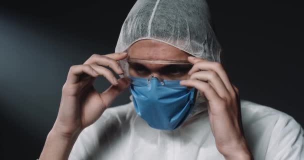 Gros plan du jeune médecin homme caucasien fatigué en pleine protection enlever les lunettes et le masque médical. Homme épidémiologiste regardant vers le bas bouleversé et déçu. Concept de coronavirus. Docteur pendant covid-19 — Video