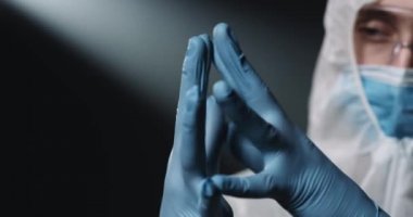 Mavi lastik eldivenli doktor epidemiyolojistin ellerini kapatın. Koruyucu kostümlü, tıbbi maskeli ve gözlüklü bir erkek doktor. Coronavirus konsepti. Covid-19 salgını.