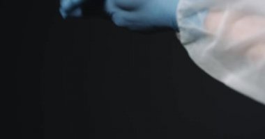 Doktorun mavi lastik eldivenleriyle ellerini kapat. Elinde dezenfektan püskürtüp siyah arka planda yayılıyor. Temizlik konsepti. Bakteriler öldürülüyor.