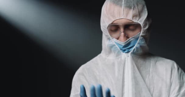 Médico epidemiologista masculino caucasiano em traje de proteção total e em máscara médica tomando luvas azuis de borracha antes de trabalhar com coronavírus. Homem médico vestindo proteção contra vírus covid-19 . — Vídeo de Stock