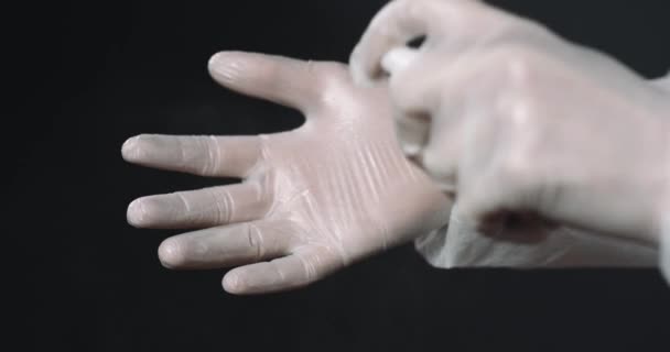 Gros plan des mains en gants de caoutchouc blanc du médecin. Pulvérisation de désinfectant sur les mains et propagation sur fond noir. Concept de nettoyage. Tuer des bactéries. — Video