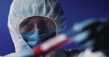 Laboratuvardaki bilim adamının elindeki cam test tüpünü koronavirüs aşısıyla kapatın. Tam teçhizatlı koruma kostümü giymiş bir adam. Kan grubu pozitif. Salgına karşı aşıların icadı.