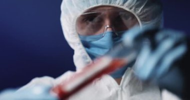 Tıbbi maskeli ve koruyucu gözlüklü, cam test tüpünü kanla tutan ve kameraya gösteren tam teçhizatlı sağlık görevlilerini kapatın. Coronavirus testi negatif. Doktor hayır der gibi başını sallıyor..