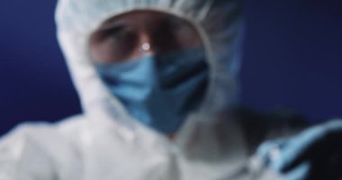 Tıbbi maskeli ve koruyucu gözlüklü, cam test tüpünü kanla tutan ve kameraya gösteren tam teçhizatlı sağlık görevlilerini kapatın. Coronavirus testi pozitif. Doktor teşhisi gösteriyor..