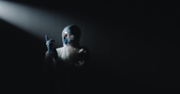 カメラの前に暗闇の中に立っている白い滅菌衣装、ゴーグル、医療用マスクで完全に装備された医療でズームし、ゴム手袋を取ります。医者はcovidから守るために. — ストック動画