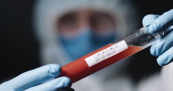 Detailní záběr zkumavky s vakcínou z koronaviru v rukou medika v chráněném kostýmu. Covid-19 pozitivní testovací koncept. Vynalézání léků z viru. Laboratorní výzkum s vakcínami. — Stock video