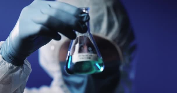 Close-up van glazen fles met vloeibaar vaccin tegen coronavirus in handen van mannelijke blanke arbeider in volledig beschermd kostuum, masker, bril en handschoenen. Laboratoriumonderzoek van vaccins. — Stockvideo