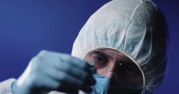 Close-up van glazen fles met vloeibaar vaccin tegen covid-19 in handen van blanke man wetenschapper in volledig beschermd kostuum, masker, bril en handschoenen. Laboratoriumonderzoek van geneesmiddelen. — Stockvideo