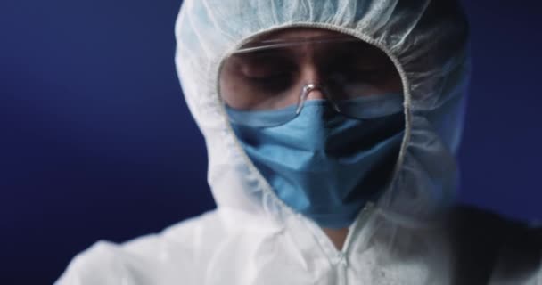 Primo piano di medico completamente attrezzato e protetto in maschera medica e occhiali che tengono la provetta di vetro con il sangue e dimostrano alla telecamera. Test di laboratorio del coronavirus. — Video Stock