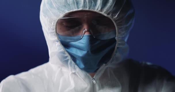 Detailní záběr plně vybaveného a chráněného lékaře v lékařské masce a brýlích, držícího skleněnou zkumavku s krví a ukazujícího před kamerou. Covid-19 pozitivní test. Diagnóza doktríny. — Stock video
