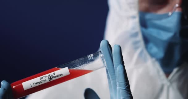 Die Nahaufnahme eines Glasröhrchens mit Blut und positivem Coronavirus führt dazu, dass die Hände in Handschuhen eines kaukasisch ausgerüsteten männlichen Arbeiters stecken. Covid-19-Labortest. — Stockvideo