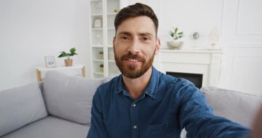 Oturma odasında kamerayla konuşan ve görüntülü sohbet eden yakışıklı beyaz adam blogcusu. Erkek video blogcusu bir şey anlatıyor ve video blogunda açıklıyor. Video blogu. Evden görüntülü hat.