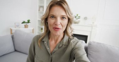 Oturma odasında kamerayla konuşan ve görüntülü sohbet eden güzel beyaz kadın blogcu POV 'u. Kadın video kaydedicisi bir şey anlatıyor ve video blogunda anlatıyor. Video blogu. Evden görüntülü hat.