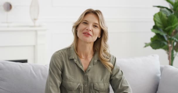 Portret van een mooie jonge blanke vrouw blogger zittend op de bank in de woonkamer en pratend met de camera. Vrouwelijke vlogger vertelt iets en legt het uit. Videoblog. Vlog van thuis. — Stockvideo