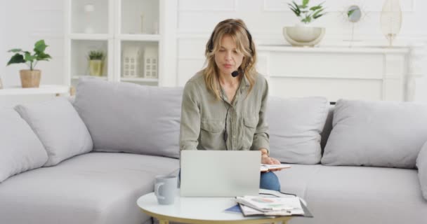 Jovem blogueira caucasiana em fone de ouvido sentado no computador portátil no sofá e falando na webcam. Feminino vlogger no microfone trabalhando, discutindo e observando. Vídeo blogging. Início vlog estudar conceito. — Vídeo de Stock