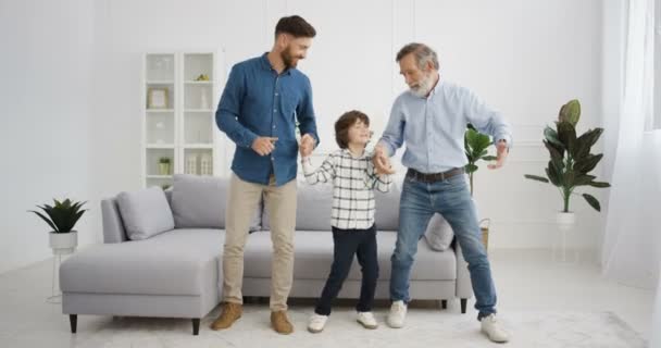Καυκάσιοι άντρες. Μικρό χαριτωμένο παιδί με τον παππού και τον πατέρα να χορεύουν και να κινούνται περίεργα στο σαλόνι. Ανώτερος άντρας με γιο και εγγονό να κρατιούνται χέρι-χέρι και να ακούνε μουσική. — Αρχείο Βίντεο