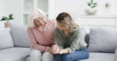 Umutsuzluk içinde kanepede oturan, evde oturup endişelenen beyaz saçlı yaşlı bir kadın ve onu sakinleştiren yaşlı bir anne. Depresyonda olan yetişkin kız, yaşlı anneyle konuşuyor. Bunalımlı umutsuz kadın.