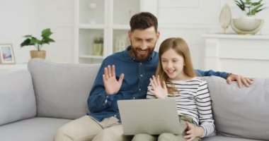 Oturma odasındaki kanepede oturan mutlu bir adam. Yanında genç bir kız ve dizüstü bilgisayarla görüntülü sohbet ediyor. Küçük kız el sallayan ve webcam 'de video sohbet eden genç, beyaz, yakışıklı bir babası var..