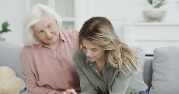 Stará bělovlasá šedovlasá matka se uklidňuje a snaží se pomoci své dospělé krásné dceři, zatímco sedí na pohovce v obývacím pokoji. Mladé zoufalství stresující žena s depresí a stresem. — Stock video