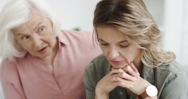 Närbild av gamla kaukasiska gråhåriga mor lugnar ner sig och försöker hjälpa sin vuxna vackra dotter medan du sitter på soffan i vardagsrummet. Ung förtvivlan ledsen kvinna som har depression och stress. — Stockvideo