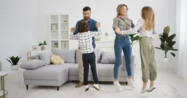 Neşeli beyaz aile dansları ve kilitleme sırasında evdeki oturma odasında eğlenmeleri. Anne ve baba küçük tatlı bir kız ve oğulla dans ediyor. Küçük çocuklar aileleriyle müzik dinliyorlar..