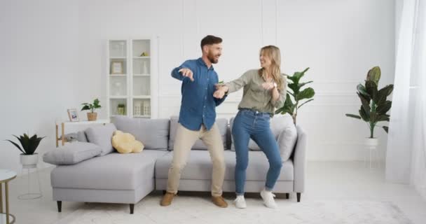 Glada vita unga roliga gifta par som har roligt och dansar i mysiga vardagsrum. Vacker lycklig kvinna och stilig man dansar och skrattar hemma. Fru och make relationer. Inomhus. — Stockvideo