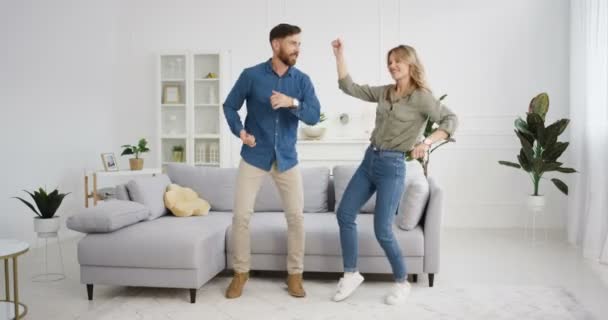 Feliz caucasiano jovem engraçado casal apaixonado se divertindo e dançando na sala de estar. Mulher bonita e homem bonito dançam e riem. Relações de namorados e namorados. Interior. — Vídeo de Stock