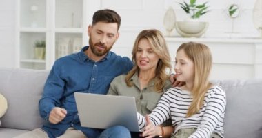 Genç beyaz anne ve babalar evlerinde kanepede oturup dizüstü bilgisayar kullanarak küçük tatlı bir kıza ders veriyorlar. Anne ve babasıyla birlikte oturma odasında bilgisayardan bir şey izleyen küçük bir kız..