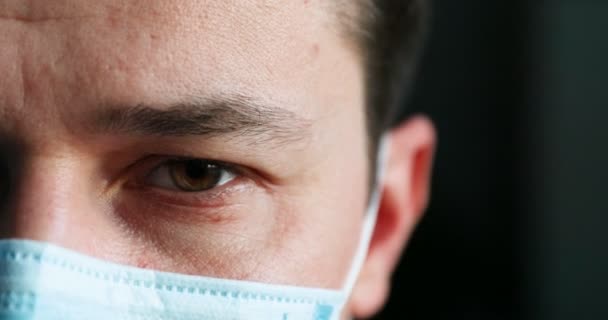 Primo piano di faccia di dottore in disperazione e umore triste. Giovane medico caucasico in maschera medica blu guardando la fotocamera con occhi stanchi e rialzati. Concetto di pandemia di coronavirus. — Video Stock