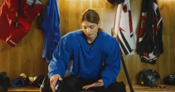 Porträt einer attraktiven kaukasischen Hockeyspielerin in blauer Uniform, die auf einer Bank in der Umkleidekabine sitzt und traurig in die Kamera blickt. Enttäuschte Sportlerin nach Niederlage in Umkleidekabine. — Stockvideo