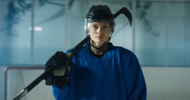 Kasklı, güzel beyaz kadın hokey oyuncusunun ve buz arenasında neşeyle gülümseyen kulübün portresi. Sopalı neşeli, güzel sporcu kadın..