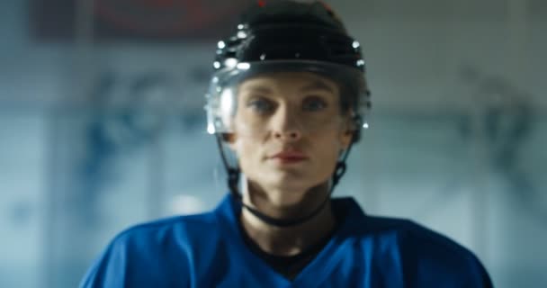 Caméra zoomant sur le visage de heureuse belle jeune joueuse de hockey caucasienne dans le casque souriant joyeusement sur l'arène de glace. Portrait de sportive. Flou à concentré. Gros plan de jolie femme. — Video