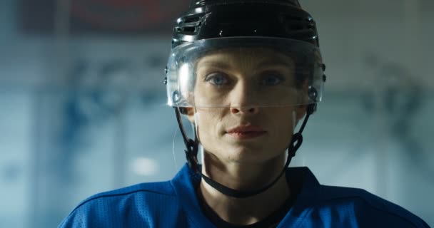 Großaufnahme der schönen jungen kaukasischen Hockeyspielerin mit Helm, die mit beängstigendem Gesicht auf der Eisarena in die Kamera blickt. Porträt einer attraktiven Sportlerin in Kaskade. — Stockvideo