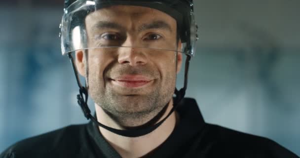 Primer plano de feliz guapo joven caucásico jugador de hockey masculino en casco sonriendo alegremente en la arena de hielo. Retrato de un deportista profesional alegre y atractivo . — Vídeos de Stock