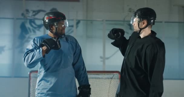 Mixed-races jonge mannelijke hockey spelers in uniformen en helmen geven vijf aan elkaar op het ijs arena na wedstrijd. portret van multi-etnische sporters glimlachend vrolijk naar camera voor wedstrijd. — Stockvideo