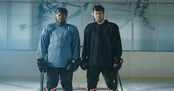 Portrait de joueurs de hockey masculins multiethniques en uniforme et casques se regardant et souriant à la caméra sur la patinoire. Sportifs mixtes en casques debout avant le match. — Video