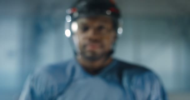 Cámara zoom en la cara de los jóvenes afroamericanos guapo jugador de hockey masculino feliz en casco y uniforme sonriendo a la cámara en la arena de hielo. Primer plano del deportista alegre durante el partido. Retrato . — Vídeos de Stock