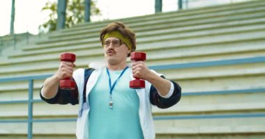 Beyaz tenli retro fitness antrenörü merdivenlerin yanında spor yapıyor. Gözlüklü, bıyıklı, caddede dambıllarla egzersiz yapan yakışıklı bir adam. Spor yaşam tarzı. 60 'ların konsepti