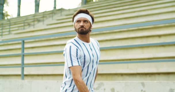 Porträt eines gutaussehenden Retro-Sportlers, der mit roten Kurzhanteln auf dem Bizeps trainiert und Muskeln im Freien zeigt. Kaukasischer Vintage-Mann mit Stirnband und lustigem Gesicht beim Training auf der Straße. Sportkonzept — Stockvideo