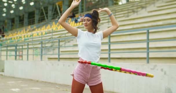 Hermosa joven atleta caucásica de cabello oscuro feliz girando una rueda de fitness mientras está de pie al aire libre. Chica deportiva bastante vintage en estilo retro haciendo ejercicios de fitness en la calle. Concepto deportivo — Vídeo de stock