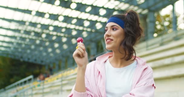 Mooie blanke vrolijke vintage vrouw in goed humeur met lolly in de hand en wegkijkend. Ouderwets mooi vrolijk meisje in roze jasje met glimlach op gezicht buiten. Portretconcept — Stockvideo