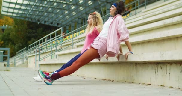 Duas belas garotas vintage caucasianas alegres fazendo tríceps empurrar para cima nas escadas ao ar livre. Atletas muito felizes do sexo feminino em estilo retro tendo treino em grupo na rua. Treinamento com parceiro. Conceito de desporto — Vídeo de Stock