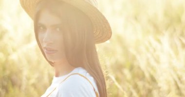 Beyaz tenli, şapkalı güzel bir kızın kameraya dönüp gün ışığında neşeli bir şekilde gülümsemesi. Arkadan bak. Güzel, büyüleyici bir kadın gülüyor, yazın çimlerin üzerinde duruyor..