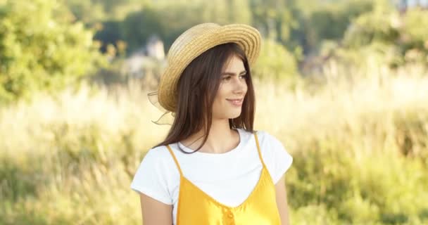 Porträtt av vacker ung brunett vit kvinna i hatt står i fält, vända ansikte mot kamera och ler glatt. Charmig lycklig flicka med leende på sommaren. Utomhus. — Stockvideo