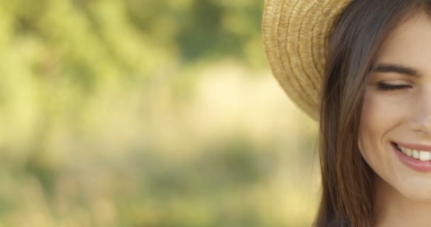 夏に屋外カメラに喜んで笑みを浮かべて帽子のかなり楽しい白人のブルネットの女の子の半分の顔のクローズアップ。自然の笑顔で良い気分で魅力的な若い女性の肖像画. — ストック動画