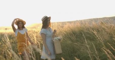 İki beyaz, güzel, stil sahibi kız. Şapkalı en iyi arkadaşlar. Bir sepet çiçekle tarlada yürüyorlar. Gün batımında doğada gezinen güzel dişiler..