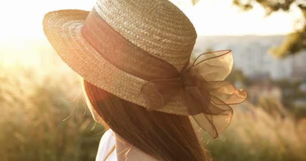Närbild av ung vit vacker flicka i hatt med lång brunett hår vända ansikte mot kamera och ler glatt på solnedgången i naturen. Porträtt av ansikte charmig kvinna i fält i utkanten. — Stockvideo